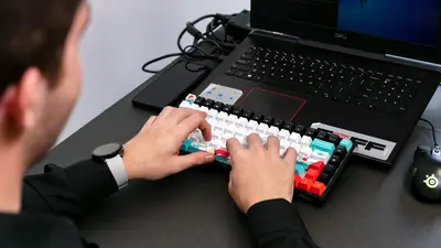 Un homme, vu de dos et partiellement cadré, laisse apparaître son côté droit, il saisit sur le clavier de son ordinateur.