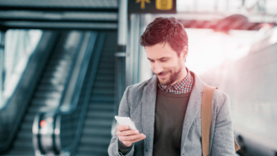 A man at an airport, looking at his phone and smiling, with a focus on cloud access security solutions.