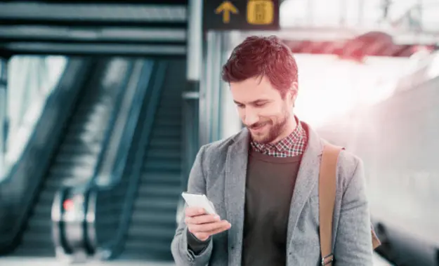 A man at an airport, looking at his phone and smiling, with a focus on cloud access security solutions.