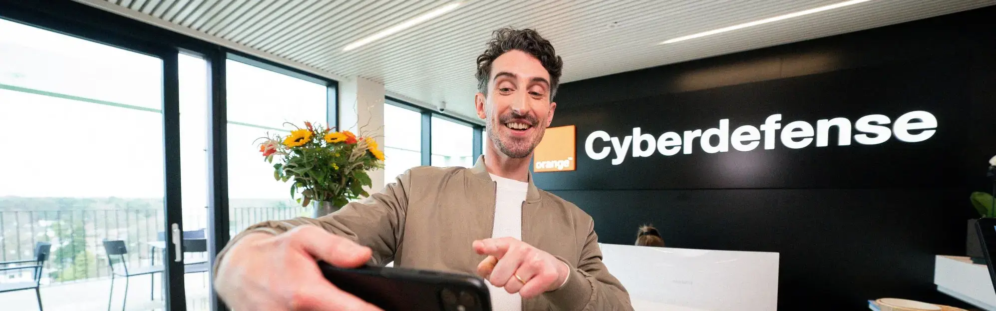 Homme en train de se prendre en photo devant l'accueil d'Orange cyberdefense