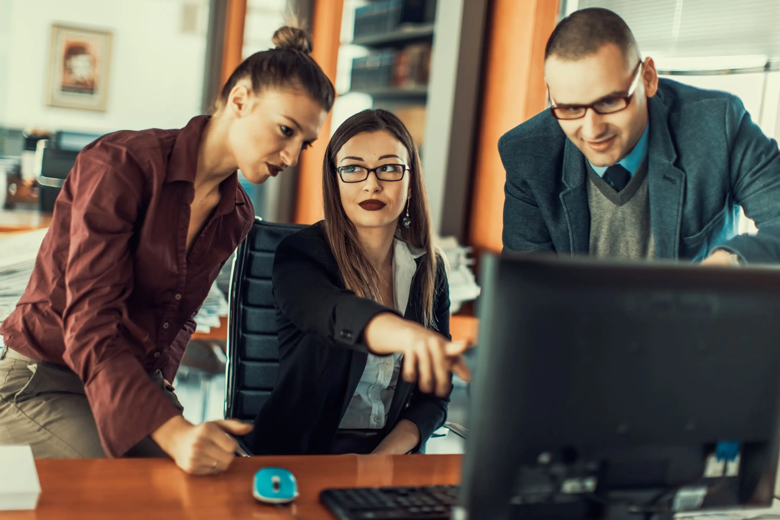 Three colleagues gathered around a computer, engaged in a discussion or collaboration.