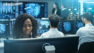A woman with other team members in the background, in a control center with data models on the screens