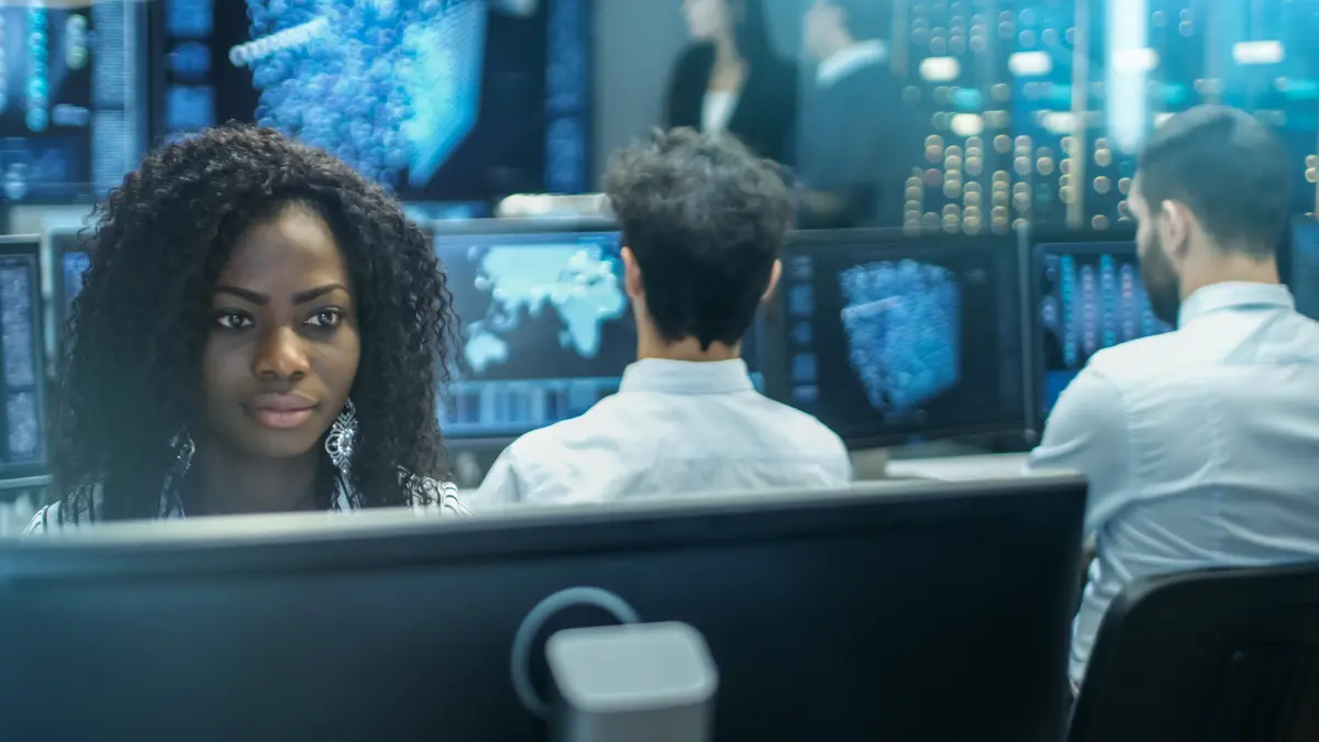 A woman with other team members in the background, in a control center with data models on the screens