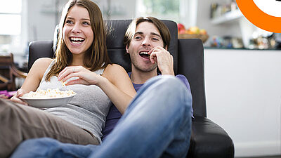 Un couple assis sur un canapé consomme du pop corn en regardant un film. 