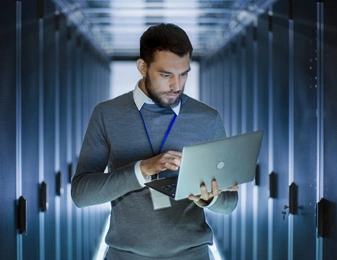 Un homme dans un data center consulte son ordinateur portable