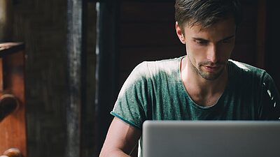 un homme assis dans un café tape sur son ordinateur portable