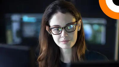 Une jeune femme portant une paire de lunettes, travaillant dans une salle informatique regarde un écran d'ordinateur. 