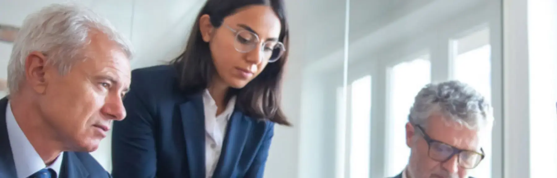 Trois professionnels en réunion regardent un écran d'ordinateur et une tablette tactile