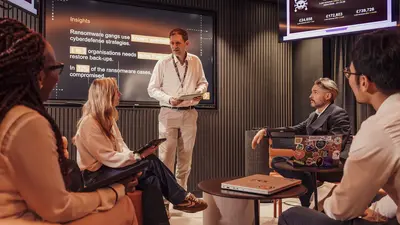 Eine Gruppe von fünf Personen in der Cyber Experience. Ein Mann steht und präsentiert, während die anderen zuhören. 