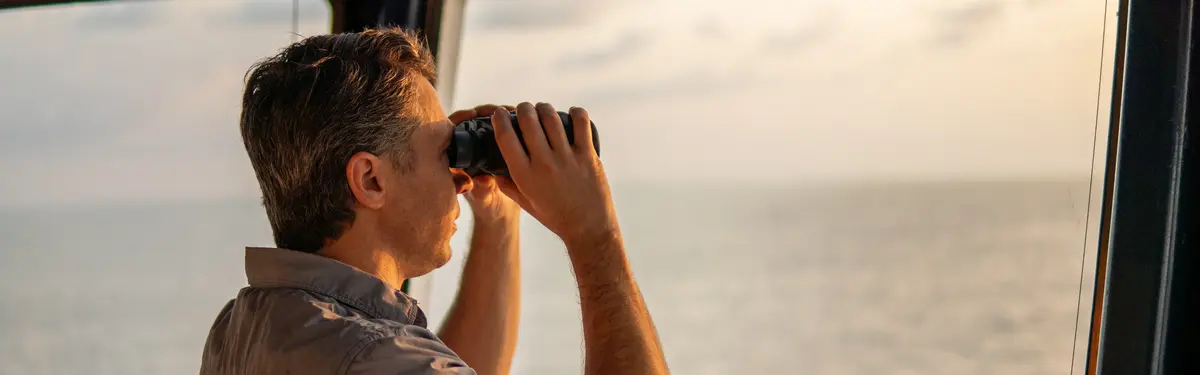A captain with binoculars looking across the ocean