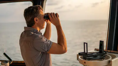 A captain with binoculars looking across the ocean