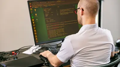 Un homme est assis de dos à un bureau, face à son ordinateur, qu’il regarde attentivement.