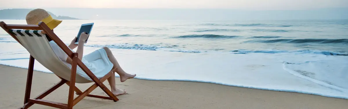 Woman in a lawnchair on the beach reading a cybersecurity article on a tablet