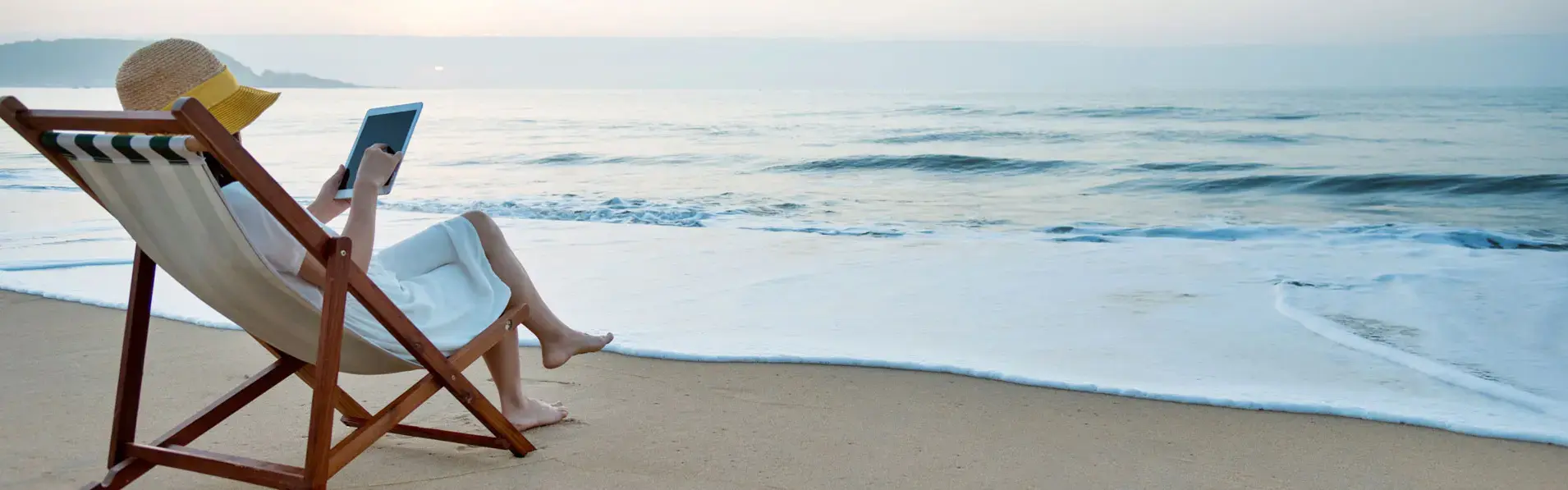 Woman in a lawnchair on the beach reading a cybersecurity article on a tablet