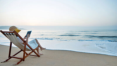 Woman in a lawnchair on the beach reading a cybersecurity article on a tablet