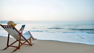 Woman in a lawnchair on the beach reading a cybersecurity article on a tablet