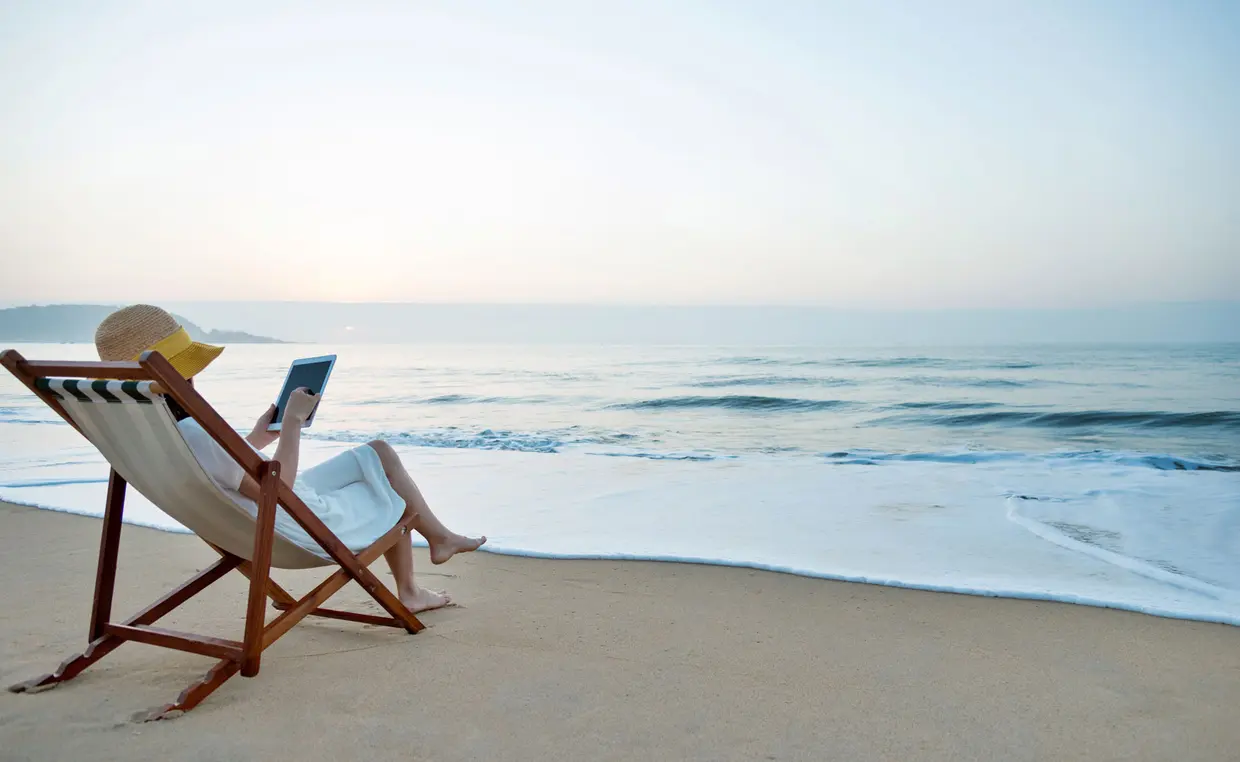 Woman in a lawnchair on the beach reading a cybersecurity article on a tablet