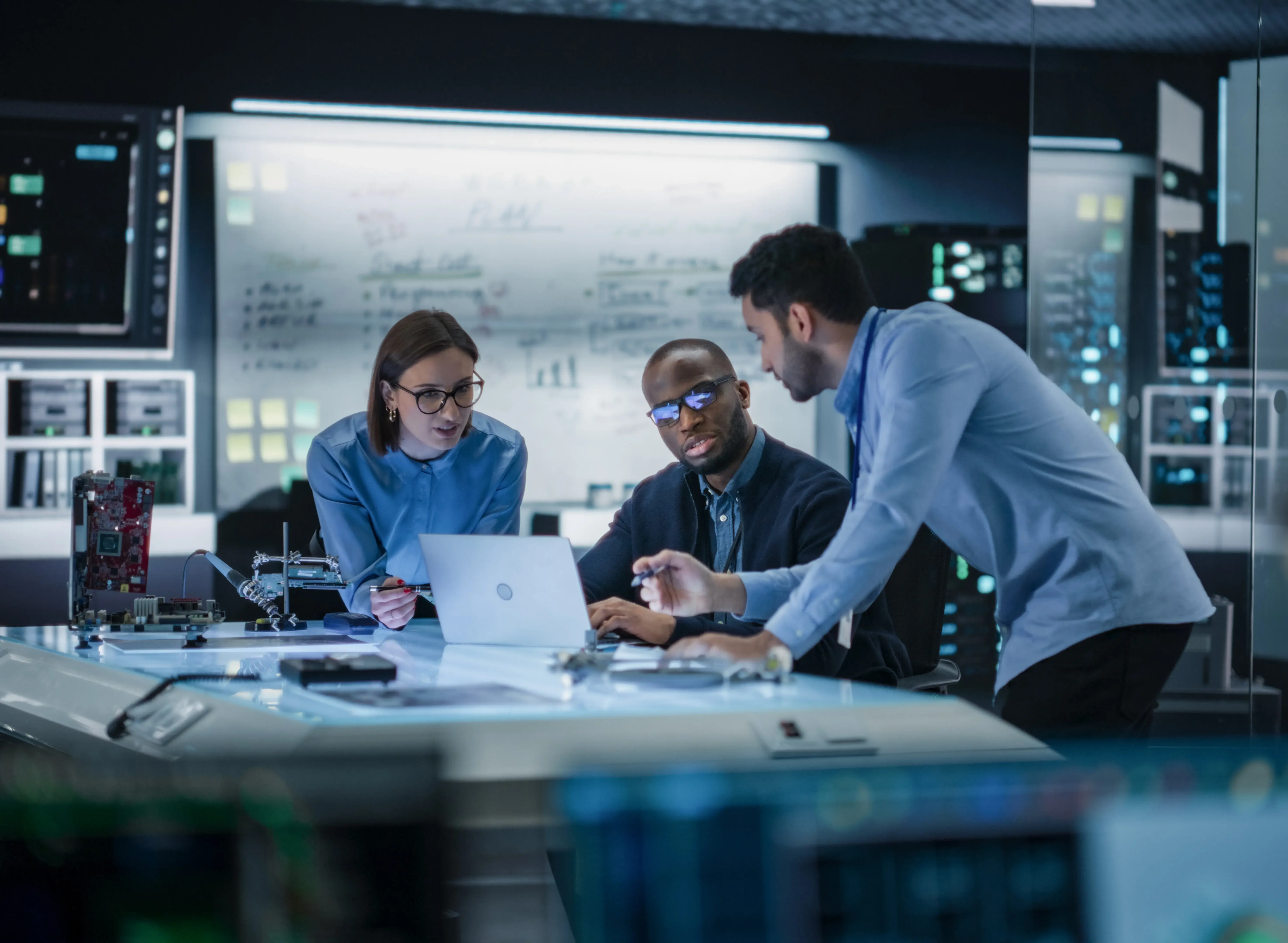 Three team members in a high technology room discussing the contents of a laptop