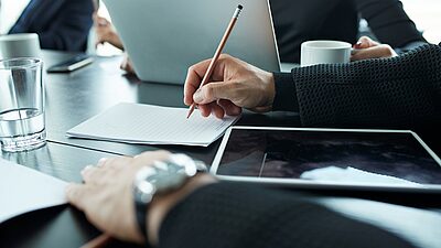 Meeting participants with hands on a table and a tablet