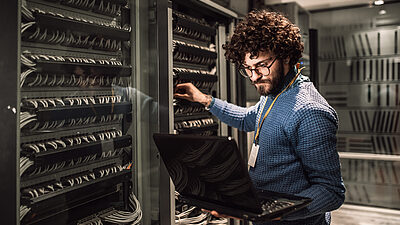 Afbeelding van een man met een laptop bij servers