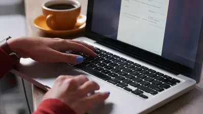 gros plan sur un pc avec des mains qui écrivent et un café à côté