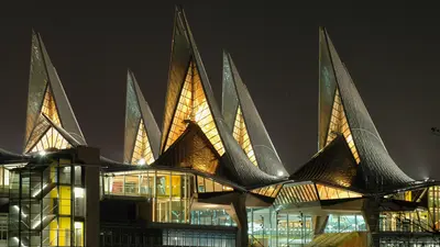 Night view of a building with illuminated pointed roofs and glass facade, glowing in the dark.