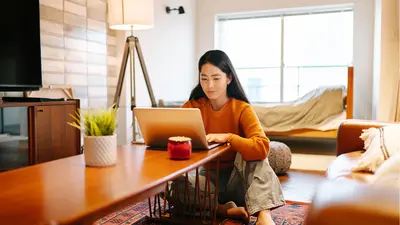Une femme assise dans son salon consulte un ordinateur