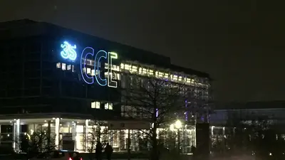 Nachtaufnahme eines modernen Gebäudes mit leuchtenden Neon-Schildern. Das Gebäude ist von dunklem Himmel und wenigen Bäumen umgeben.
