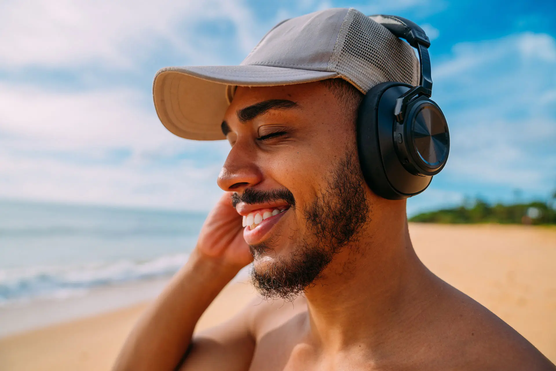 A tanned man with headphones enjoying a cyber security podcast on a beach