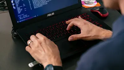 Un homme est assis à son bureau, vu de dos et partiellement cadré, en train de taper sur son ordinateur.