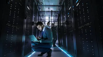 Data engineers kneeling with laptop in server room