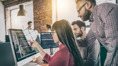 Three developers around a computer monitor reviewing code