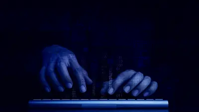 Close-up of a hooded figure in a dark environment, surrounded by digital code and cybersecurity interface elements