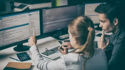 Two team members discussion items on multiple monitors