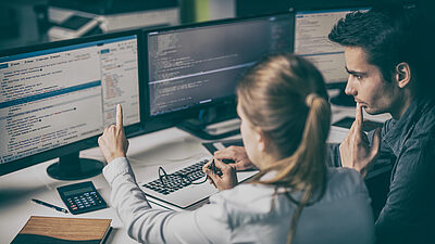 Two team members discussion items on multiple monitors