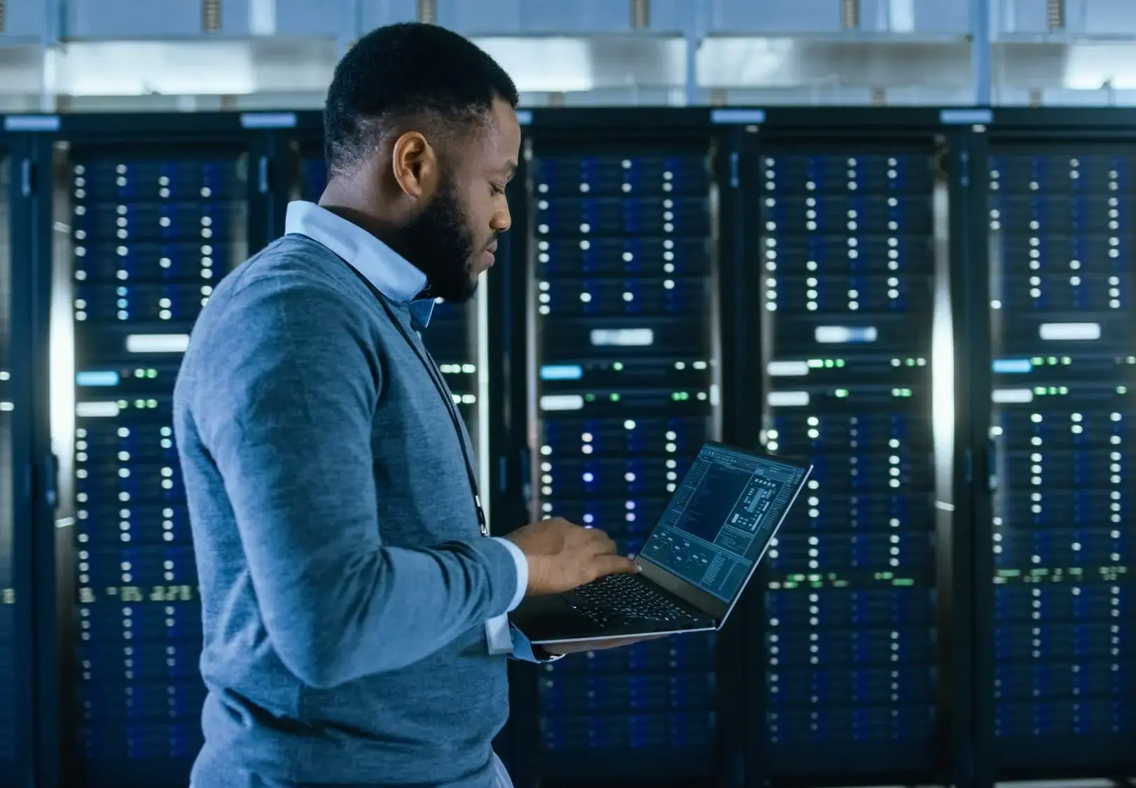 A person working in a data center or server room, using a laptop to monitor or manage the servers.