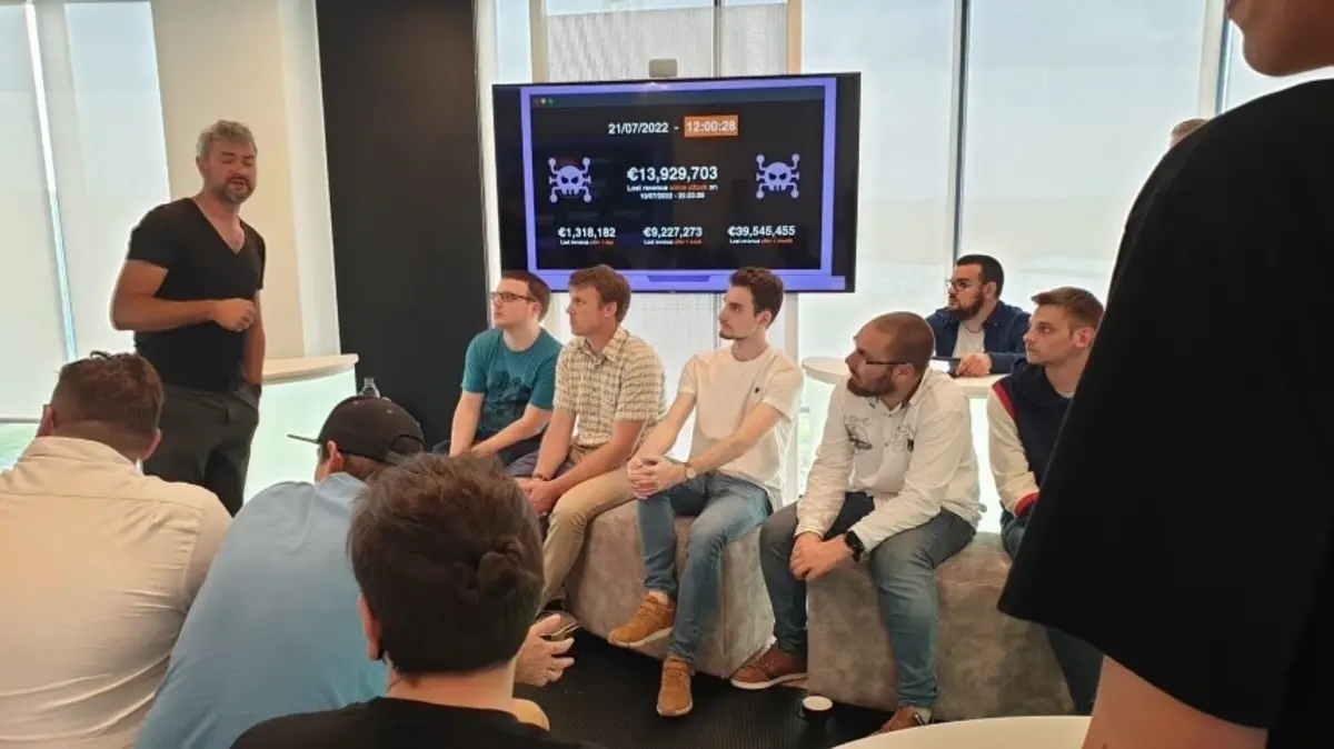 Group of people in a conference or meeting room, some standing and some seated, with a presentation screen in the background.