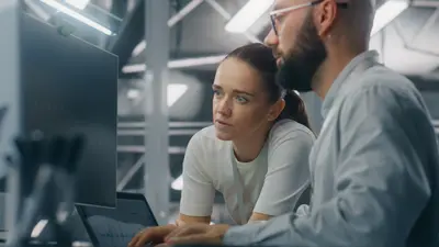 Ein Team aus männlichen und weiblichen IT-Ingenieuren, die gemeinsam vor einem Computerbildschirm wichtige Kennzahlen zur Netzwerkleistung auswerten. Teamarbeit und IT-Überwachung in Echtzeit.