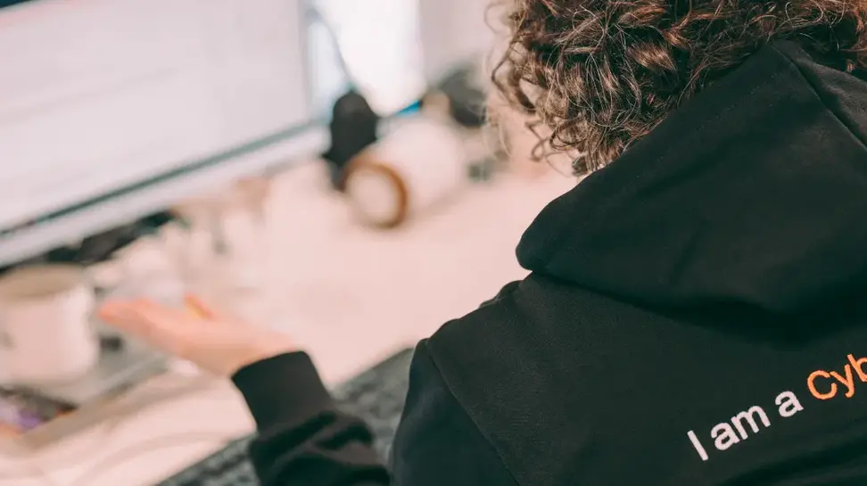 Person with an Orange Cyberdefense hoodie sitting in front of a computer