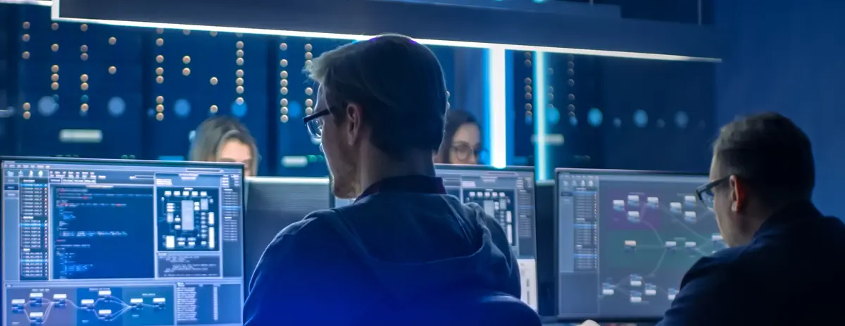 Cybersecurity professionals working in a data center with multiple screens showing code and data.