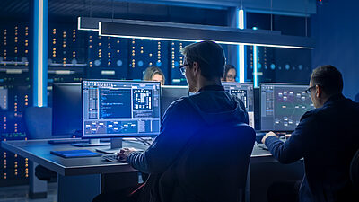 Cybersecurity professionals working in a data center with multiple screens showing code and data.