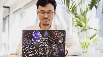 Ein Mann arbeitet an einem Laptop, der mit bunten Stickern beklebt ist.