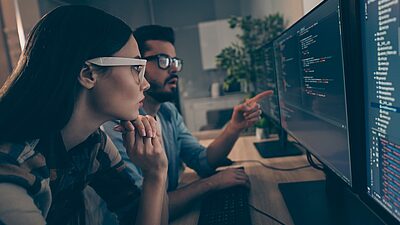 Two developers looking at multiple screens and analyzing lines of code
