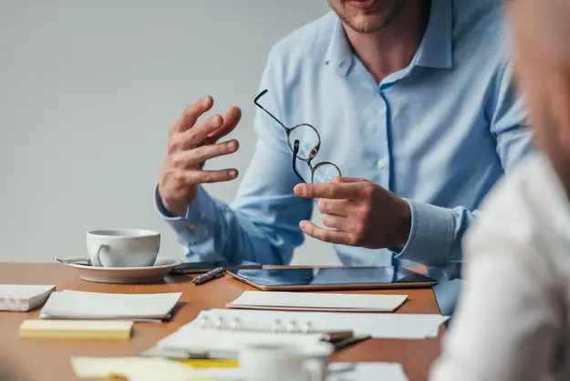 Close-up of a consultant gesturing during a meeting, with documents and a tablet on the table