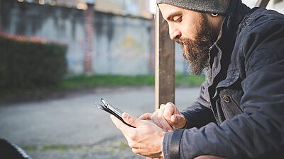 Man wearing a beanie, sitting down, seen from the side, looking down at his phone