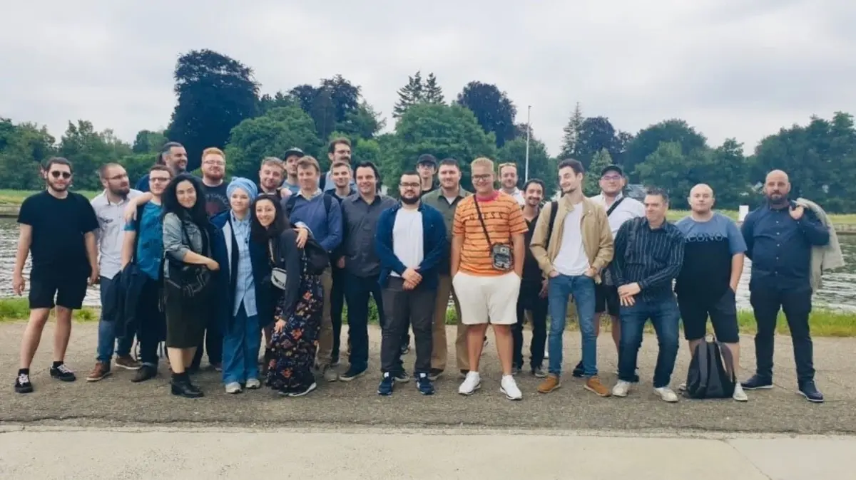 Group of people standing outdoors, posing for a photo, some with arms crossed.