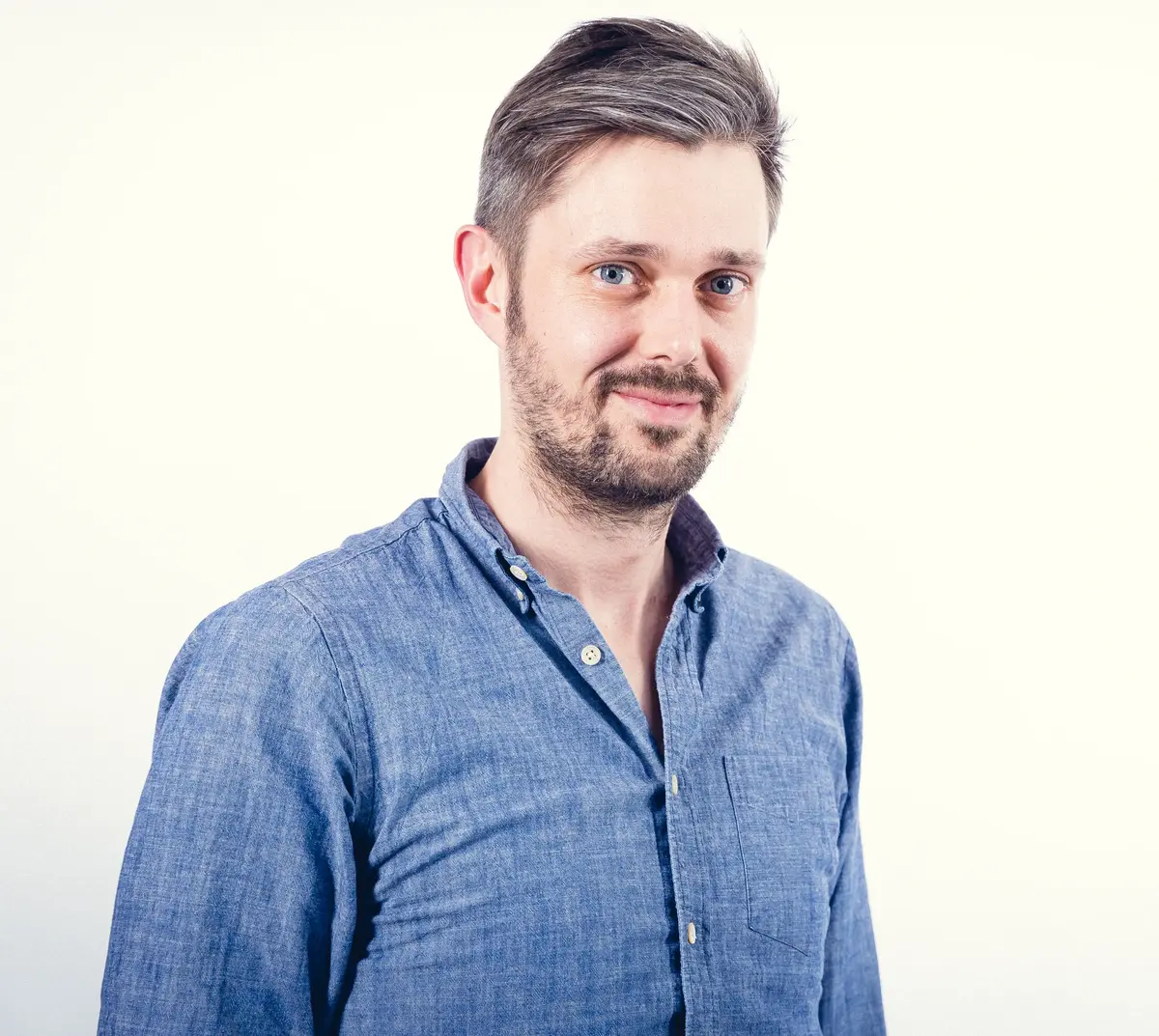 Portrait of a man with short dark hair and a beard, wearing a patterned shirt, smiling at the camera.