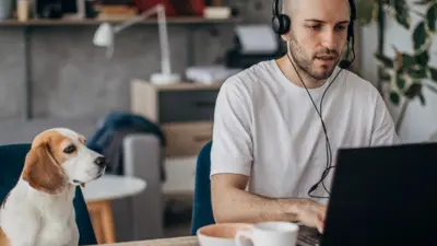 Man with headphones working from home with his dog by his side