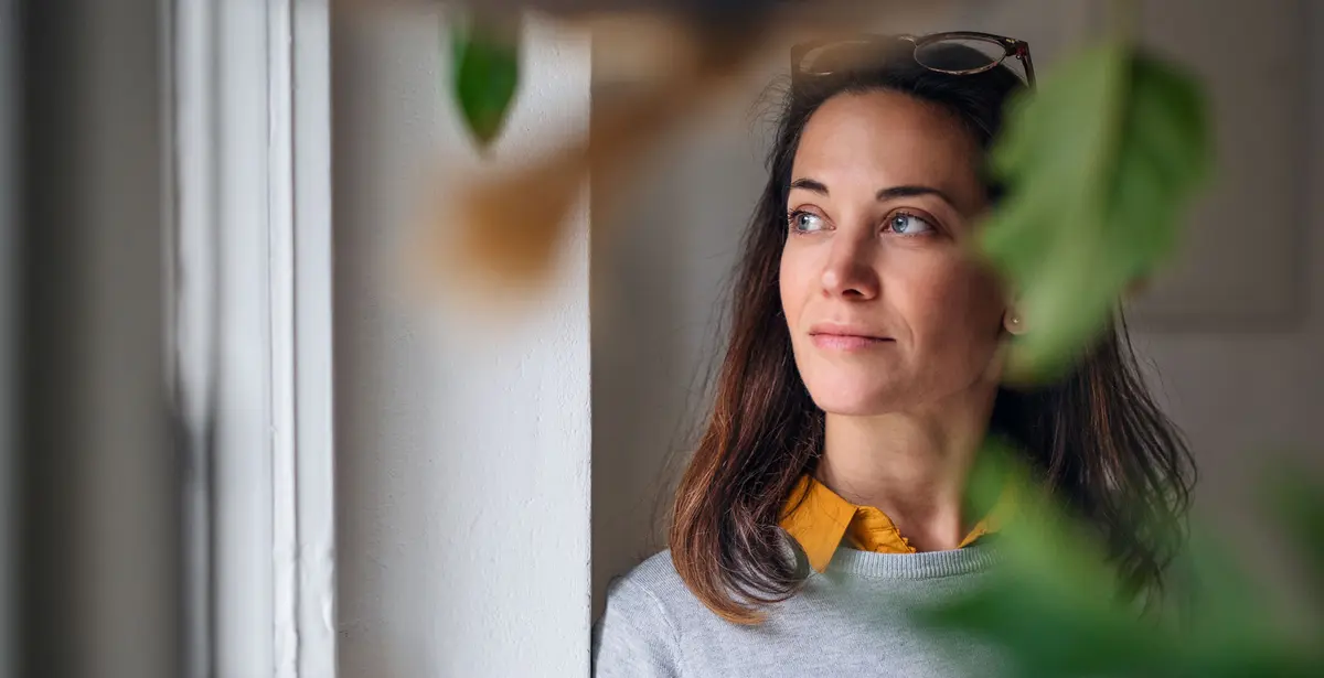 Woman holding a coffee cup while looking out of a window.
