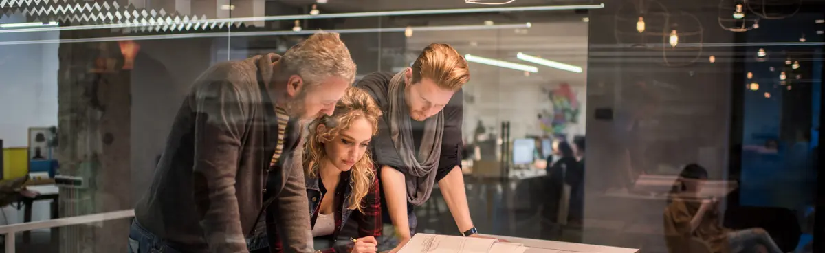 Three team members standing at a table reviewing blueprints
